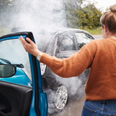 Anscheinsbeweis: Frau von hinten, die nach einem Auffahrunfall aus einem Auto aussteigt. Das vordere Auto raucht.