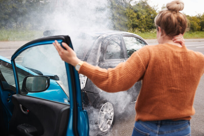 Anscheinsbeweis: Frau von hinten, die nach einem Auffahrunfall aus einem Auto aussteigt. Das vordere Auto raucht.