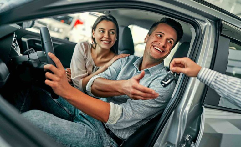 Ein Fahrer und eine Beifahrerin sitzen in einem neuen Auto. Dem Fahrer wird der Autoschlüssel überreicht.