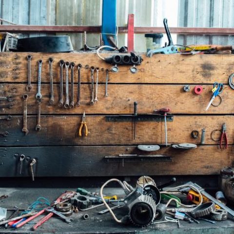 Verschiedene Werkzeuge liegen durcheinander in der Werkstatt der Garage. Alte Schraubenschlüssel hängen an der Holzwand darüber.