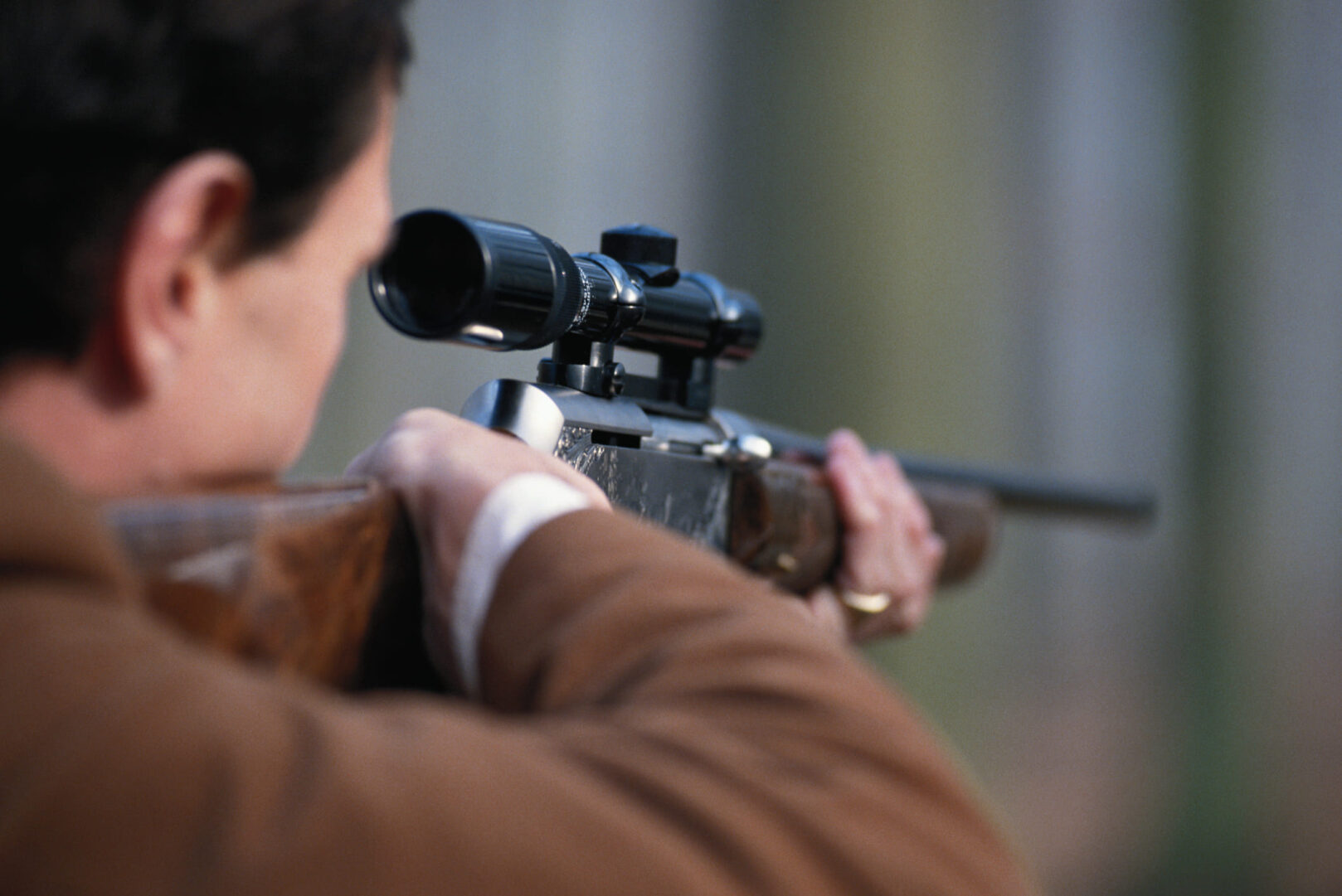 Waffengesetz Schusswaffen: Wir blicken einem Mann über die Schulter, der durch das Zielfernrohr einer Schusswaffe blickt.