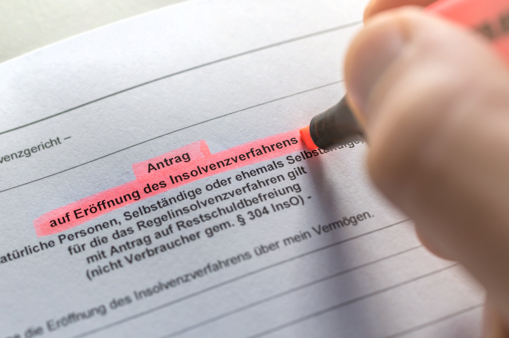 Antrag zur Insolvenzbekanntmachung in Papierform und eine Hand, die mit einem pinken Marker den Text markiert.