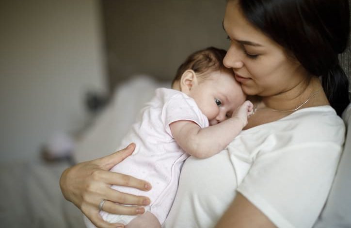 Eine junge Frau sitzt auf dem Sofa und hat ein Baby auf ihrer Brust liegen.