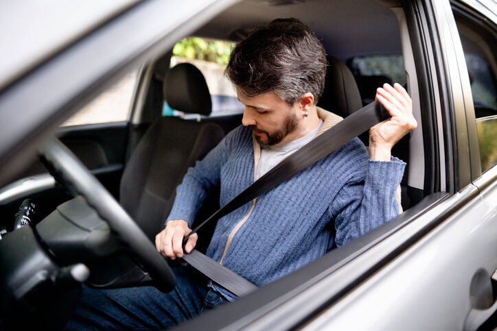Ein Mann sitzt im Auto und schnallt sich gemäß Anschnallpflicht an.