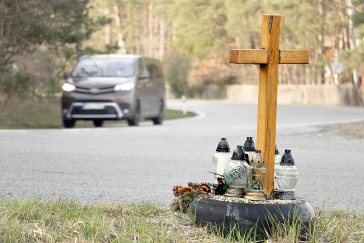 Ein Kreuz mit Kerzen an einem Unfallort in einem Land ohne Tempolimit, im Hintergrund ein Fahrzeug.