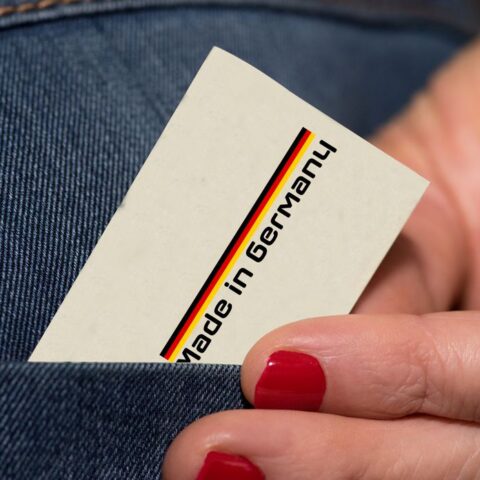 Hand mit lackierten Nägeln zieht eine Karte mit Made in Germany aus einer Hosentasche