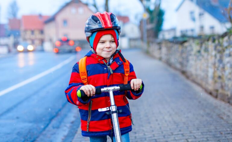 Ein Kind im Straßenverkehr auf einem Roller, mit Helm und Jacke.
