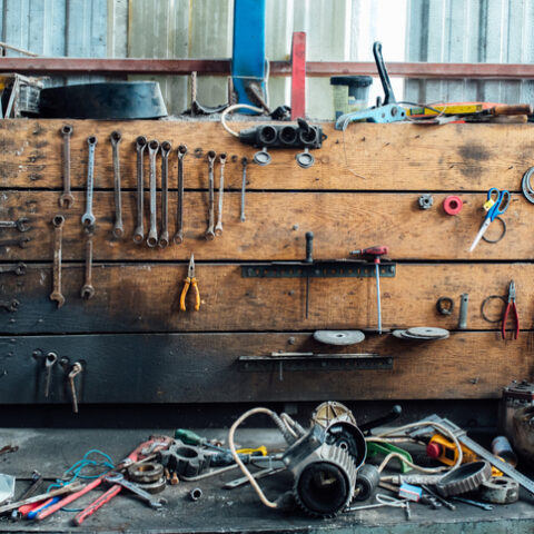 Verschiedene Werkzeuge liegen beim Garage aufräumen durcheinander in der Werkstatt der Garage. Alte Schraubenschlüssel hängen an der Holzwand darüber.