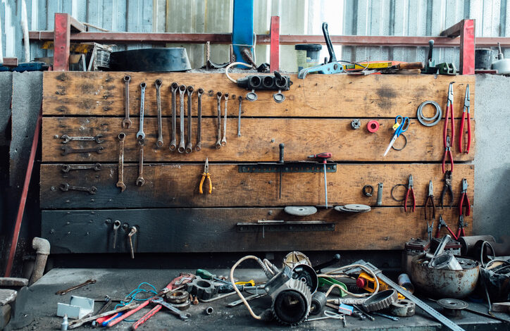 Verschiedene Werkzeuge liegen beim Garage aufräumen durcheinander in der Werkstatt der Garage. Alte Schraubenschlüssel hängen an der Holzwand darüber.
