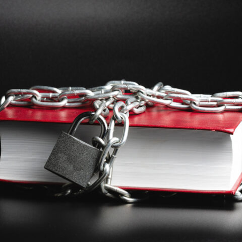 Preisgebunden: Ein rotes Buch auf dem Tisch, in Ketten gelegt, mit einem Vorhängeschloss.