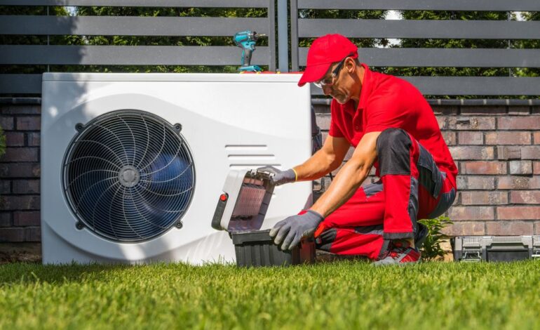 Nach § 14a EnWG baut ein Netzbetreiber in roter Arbeitskleidung ein Außengerät einer Wärmepumpe um. Er hat einen Werkzeugkoffer dabei und auf dem Gerät ist ein Akkuschrauber abgestellt.